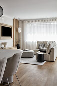 Open living room in coastal style with white columned dining table in 80s style, upholstered chairs and cream colored sofa