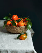 fresh tangerines in a bowl of vines on a linen tablecloth