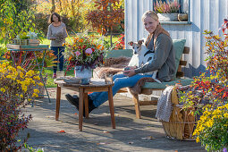 Zwei Frauen auf herbstlicher Terrasse mit Hund und Blumendekoration