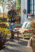 Woman places autumn bouquet of zinnias (Zinnia), roses, autumn asters on garden table