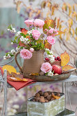 Herbstlicher Blumenstrauß aus Schneebeere (Symphoricarpos), Rosen und Herbstlaub auf Regal