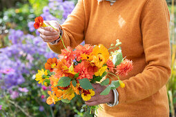Frau hält Blumenstrauss in der Hand aus Dahlien (Dahlia), Ringelblumen (Calendula) und Kapuzinerkresse (Tropaeolum)