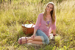 Blonde Frau in rosa Bluse und Jeans-Caprihose mit Picknickkorb auf der Wiese