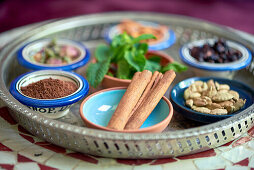Verschiedene Kräuter und Gewürze für orientalische Gerichte in kleinen Schalen, im Vordergrund Ceylon-Zimtstangen