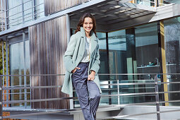 Young brunette woman in a silk blouse, blue trousers and a light blue coat