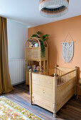 Crib next to bamboo shelf in front of apricot-colored wall