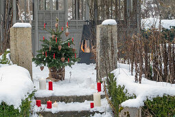 Geschmückter Christbaum mit Wachskerzen auf verschneiter Terrasse und Winterfeuer