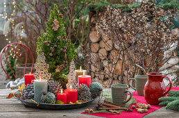 Weihnachtsdeko am Terrassentisch mit Kerzen, Kaffeetassen, Christbaumkugeln, Zapfen, Zimtstangen und Nüssen