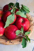 Holzschale mit roten Äpfeln auf gefliestem Küchentisch