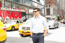 Young man with sunglasses in dark suit pants and a light shirt stands on the street