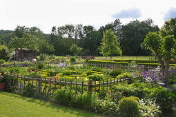 Cottage garden formally laid out inside wooden fence with vegetables and flowers