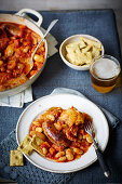 Hot-Pot mit Hähnchen, Wurst, weißen Bohnen, Tomaten, dazu Bier und Crackern