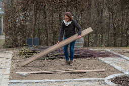 Frau bei Anlage eines Gemüsebeets mit Holzbrettern und Weidenzweigen als Rankhilfe für Kletterpflanzen