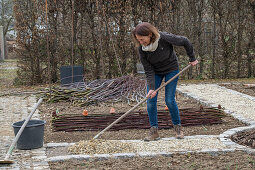 Frau bei Anlegen eines Gemüsebeets mit Flechtwand aus Weidenzweigen und Weg anlegen mit Kies