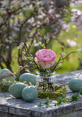 Rose blossom (pink) with branches in vase and Easter eggs on garden table