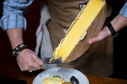 Man scraping melted, traditional Swiss raclette cheese onto plate