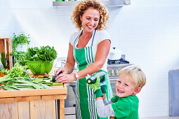Frau schneidet grünes Gemüse und Salat mit ihrem Sohn zu, Küche
