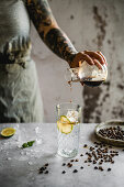 Preparation of espresso tonic, person pours coffee into a glass with tonic and lime