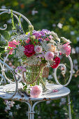 Bouquet of roses, wild carrot, flowering oregano, vetch, autumn anemone and bearded flower on iron chair