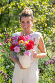 Frau trägt Vase mit buntem Strauß aus Dahlien (Dahlia), orientalischen Knöteriche (Persicaria orientalis), Bartblume (Caryopteris), und Borretsch