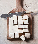 Portioned pieces of paneer on a wooden board with a knife