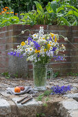 Bouquet of delphinium, dyer's chamomile (Anthemis tinctoria), tiered onion, carrot, on garden wall in beer mug