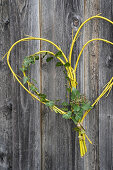 Heart-shaped door wreath made of yellow branches and ivy on a wooden wall