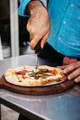 Mann schneidet Pizza Margherita mit Pizzaroller