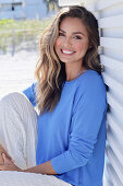 Woman in blue jumper and white trousers sitting on veranda