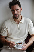 Man in cream-colored polo shirt enjoying espresso