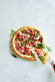 Pizza with prosciutto, rocket, onions and olives