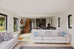 Open-plan living area with light grey sofas and modern kitchen in the background