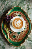 Cappuccino with latte art decorated with red flower on tray