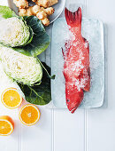 Red coral fish on ice with cabbage, Jerusalem artichokes and oranges