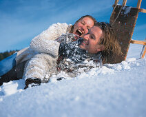 Man and woman sliding in snow on sled, laughing