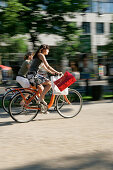 Two young women cycling along a road, Unter den Linden near Friedrichstrasse, Berlin, Germany