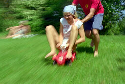 Young man pushing young woman on a toy car