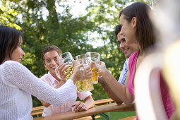 Four young people toasting each other in beer garden, Munich, Bavaria