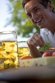 Junger Mann mit Brotzeit und Bier in Biergarten beim Starnberger See, Bayern, Deutschland