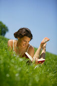 Young Woman reading book on lawn, Young Woman lying in meadow and reading a book, Bavaria