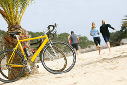 Three people on a cycle tour on the beach of cala santanyi, Majorca, Balearic Islands, Spain