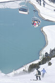Skifahrer auf der Piste und Skilift, Stausee im Hintergrund, Kühtai, Tirol, Österreich