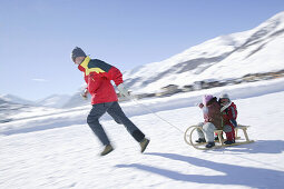 Father pulling two children on a sledge, Livigno, Italy