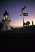 Menschen im Abendrot mit Leuchtturm und Wegweisern, Cape Reinga Kap, nördlichster Punkt Neuseelands, Nordinsel, Neuseeland
