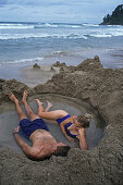Young couple bathing in hot water on the beach, Coromandel Peninsula, North Island, Oceania