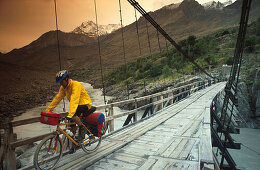 Young man mountainbiking over rope bridge, Hunza Valley, Karakorum Highway, Pakistan