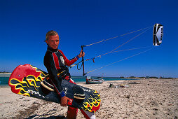 Kitesurfer walking along the beach with his board and kite, Djerba, Tunesia