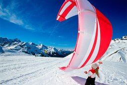 Young woman preparing kite for kiteboarding in snow, Lermoos, Lechtaler Alpen, Tyrol, Austria