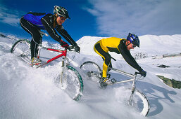 Young couple riding mountain bikes across snow, Serfaus, Tyrol, Austria