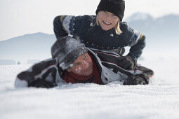 Boy lying on fathers back on snow